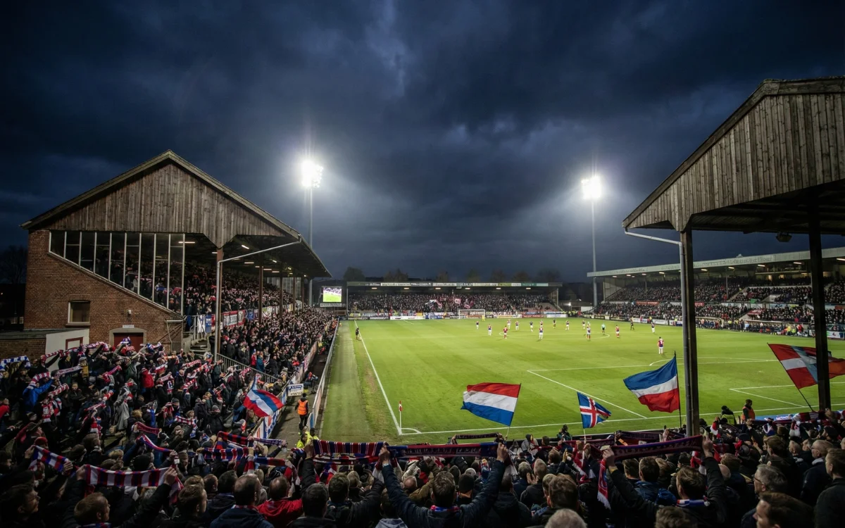 Petit stade de football europ&eacute;en avec une ambiance intime et des supporters passionn&eacute;s lors d'un match nocturne